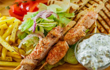 Yunan tavuk Souvlaki salata, patates kızartması patates, pide ve tzatziki sos ahşap plaka üzerinde