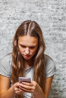 genç genç gri duvar arka plan üzerinde cep telefonu kullanarak uzun saçlı esmer kız portresi