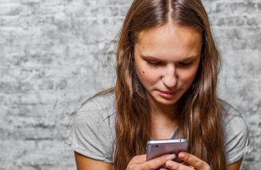 genç genç gri duvar arka plan üzerinde cep telefonu kullanarak uzun saçlı esmer kız portresi