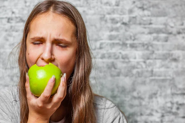 長い髪の若い 代のブルネットの少女の肖像画は 灰色の壁の背景に緑のリンゴを食べる — ストック写真