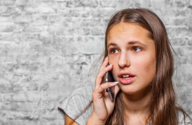 genç genç gri duvar arka plan üzerinde cep telefonu kullanarak uzun saçlı esmer kız portresi