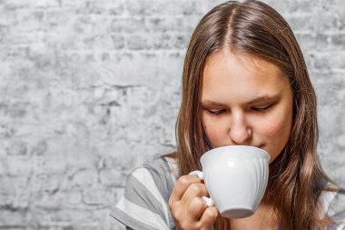bir fincan kahve ya da çay gri duvar arka planda tutarak uzun saçlı Genç Genç esmer kız portresi