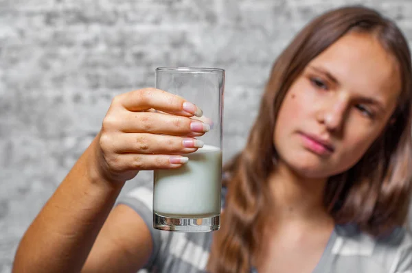 灰色の壁の背景に牛乳のガラスを保持している長い髪の若い 代のブルネットの少女の肖像画 — ストック写真