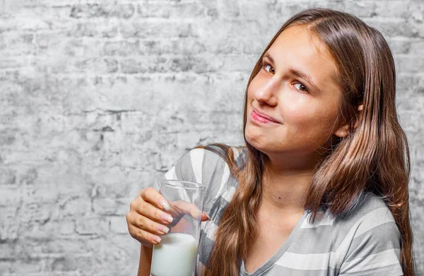 灰色の壁の背景に牛乳のガラスを保持している長い髪の若い 代のブルネットの少女の肖像画 — ストック写真