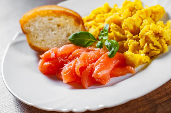 Scrambled eggs with smoked salmon and toast in white plate on wooden table background
