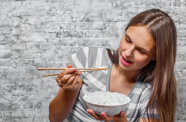 灰色の壁の背景にご飯を食べて長い髪の 代の若いブルネットの少女の肖像画 — ストック写真