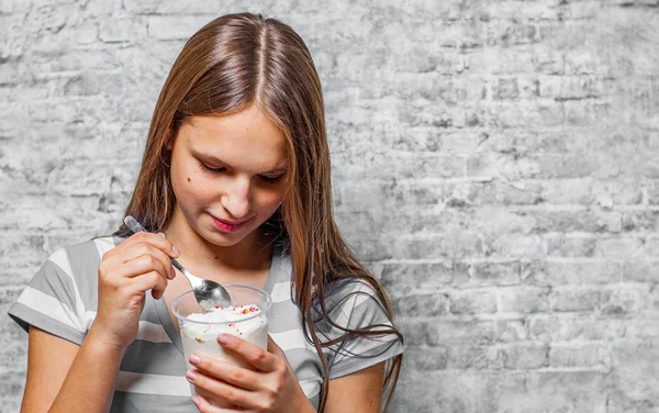 灰色の壁の背景にアイスクリームを食べる長い髪の 代の若いブルネットの少女の肖像画 — ストック写真
