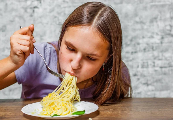 年轻的少年黑发女孩的肖像与长发吃意大利面意大利面与奶酪在灰色墙壁背景 — 图库照片