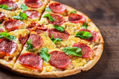 Mozzarella peynirli biberli pizza, salam, domates sosu, biber, baharat ve taze fesleğen. İtalyan pizzası ahşap masa arkasında