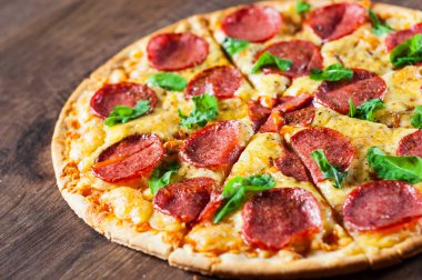 Mozzarella peynirli biberli pizza, salam, domates sosu, biber, baharat ve taze fesleğen. İtalyan pizzası ahşap masa arkasında