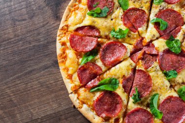 Mozzarella peynirli biberli pizza, salam, domates sosu, biber, baharat ve taze fesleğen. İtalyan pizzası ahşap masa arkasında