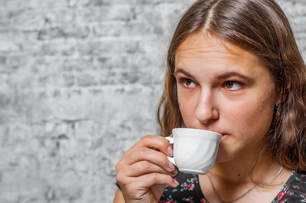 灰色の壁の背景にコーヒー エスプレッソのカップを保持している長い髪の若い 代のブルネットの少女の肖像画 — ストック写真