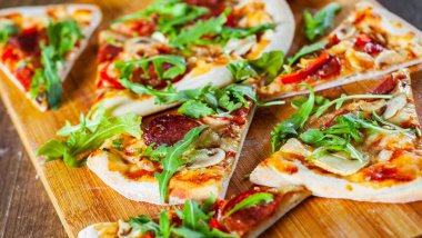 Pizza Mozzarella peyniri, mantar, biber, domates sosu, salam, biber, baharat ve taze roka ile dilim. Ahşap masa arka plan üzerinde İtalyan pizza