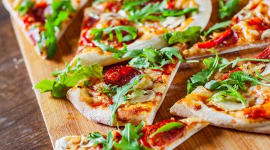 Pizza Mozzarella peyniri, mantar, biber, domates sosu, salam, biber, baharat ve taze roka ile dilim. Ahşap masa arka plan üzerinde İtalyan pizza