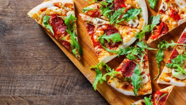 Pizza Mozzarella peyniri, mantar, biber, domates sosu, salam, biber, baharat ve taze roka ile dilim. Ahşap masa arka plan üzerinde İtalyan pizza