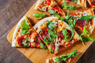 Pizza Mozzarella peyniri, mantar, biber, domates sosu, salam, biber, baharat ve taze roka ile dilim. Ahşap masa arka plan üzerinde İtalyan pizza