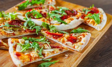Pizza Mozzarella peyniri, mantar, biber, domates sosu, salam, biber, baharat ve taze roka ile dilim. Ahşap masa arka plan üzerinde İtalyan pizza