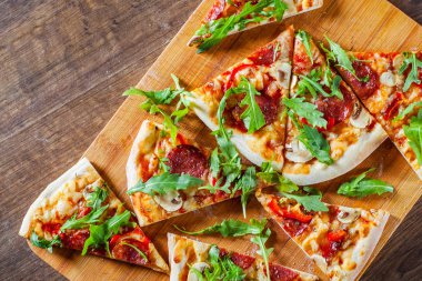 Pizza Mozzarella peyniri, mantar, biber, domates sosu, salam, biber, baharat ve taze roka ile dilim. Ahşap masa arka plan üzerinde İtalyan pizza