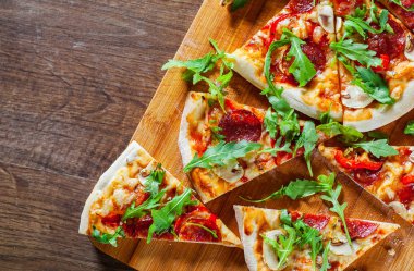 Pizza Mozzarella peyniri, mantar, biber, domates sosu, salam, biber, baharat ve taze roka ile dilim. Ahşap masa arka plan üzerinde İtalyan pizza