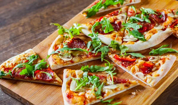 Pizza Mozzarella peyniri, mantar, biber, domates sosu, salam, biber, baharat ve taze roka ile dilim. Ahşap masa arka plan üzerinde İtalyan pizza