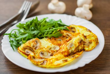 Omlet mantar ve ahşap masa arka plan üzerinde beyaz plaka roka salatası.