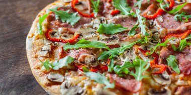 Pizza Mozzarella peyniri, mantar, jambon, domates sosu, salam, biber, baharat ve taze roka. Ahşap masa arka plan üzerinde İtalyan pizza
