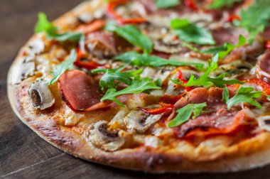 Pizza Mozzarella peyniri, mantar, jambon, domates sosu, salam, biber, baharat ve taze roka. Ahşap masa arka plan üzerinde İtalyan pizza
