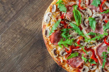 Pizza Mozzarella peyniri, mantar, jambon, domates sosu, salam, biber, baharat ve taze roka. Ahşap masa arka plan üzerinde İtalyan pizza
