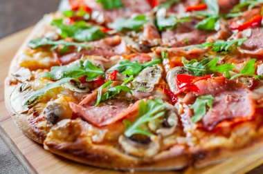 Pizza Mozzarella peyniri, mantar, jambon, domates sosu, salam, biber, baharat ve taze roka. Ahşap masa arka plan üzerinde İtalyan pizza