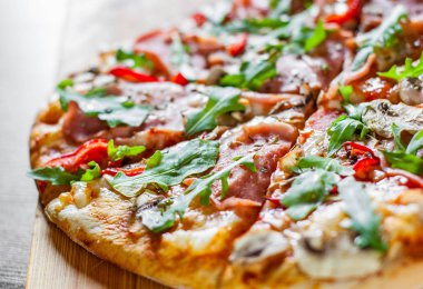 Pizza Mozzarella peyniri, mantar, jambon, domates sosu, salam, biber, baharat ve taze roka. Ahşap masa arka plan üzerinde İtalyan pizza