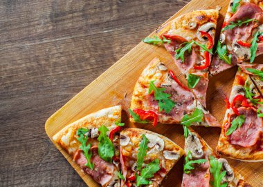Pizza Mozzarella peyniri, mantar, jambon, domates sosu, salam, biber, baharat ve taze roka ile dilim. Ahşap masa arka plan üzerinde İtalyan pizza