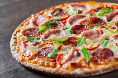 Mozzarella peynirli, jambonlu, domates soslu, salamlı, biberli, baharatlı ve taze roka soslu pizza. İtalyan pizzası ahşap masa arkasında