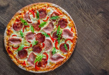 Mozzarella peynirli, jambonlu, domates soslu, salamlı, biberli, baharatlı ve taze roka soslu pizza. İtalyan pizzası ahşap masa arkasında