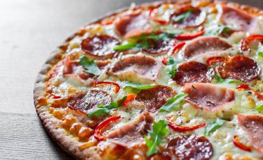 Mozzarella peynirli, jambonlu, domates soslu, salamlı, biberli, baharatlı ve taze roka soslu pizza. İtalyan pizzası ahşap masa arkasında