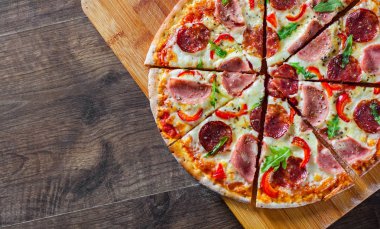 Mozzarella peynirli, jambonlu, domates soslu, salamlı, biberli, baharatlı ve taze roka soslu pizza. İtalyan pizzası ahşap masa arkasında