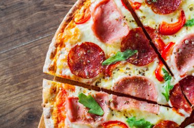 Mozzarella peynirli, jambonlu, domates soslu, salamlı, biberli, baharatlı ve taze roka soslu pizza. İtalyan pizzası ahşap masa arkasında