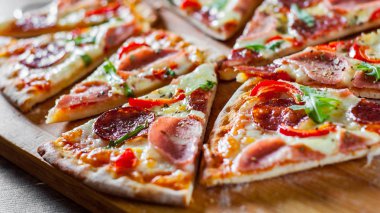 Mozzarella peynirli, jambonlu, domates soslu, salamlı, biberli, baharatlı ve taze roka soslu pizza. İtalyan pizzası ahşap masa arkasında