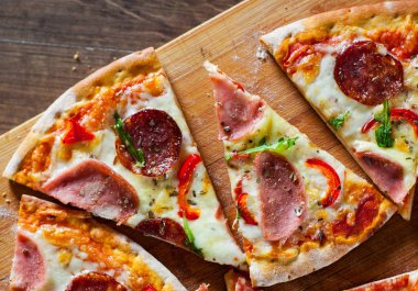 Mozzarella peynirli, jambonlu, domates soslu, salamlı, biberli, baharatlı ve taze roka soslu pizza. İtalyan pizzası ahşap masa arkasında