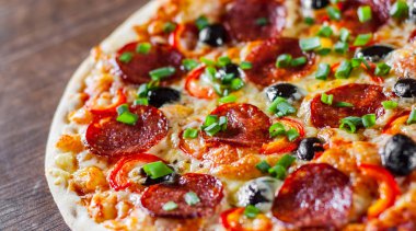 Pizza Mozzarella peyniri, sucuk, domates, biber, zeytin, salam. Ahşap masa arka plan üzerinde İtalyan pizza