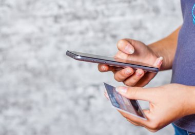 Bir kredi kartı tutan ve online alışveriş için smartphone kullanarak yakın çekim kadının eller