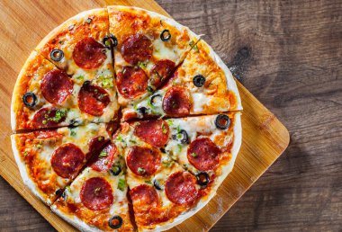 Pizza Mozzarella peyniri, sucuk, domates, biber, zeytin, salam. Ahşap masa arka plan üzerinde İtalyan pizza