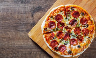 Pizza Mozzarella peyniri, sucuk, domates, biber, zeytin, salam. Ahşap masa arka plan üzerinde İtalyan pizza