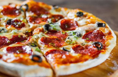 Pizza Mozzarella peyniri, sucuk, domates, biber, zeytin, salam. Ahşap masa arka plan üzerinde İtalyan pizza