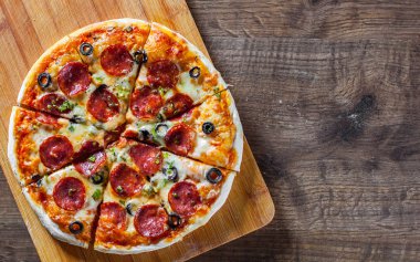 Pizza Mozzarella peyniri, sucuk, domates, biber, zeytin, salam. Ahşap masa arka plan üzerinde İtalyan pizza