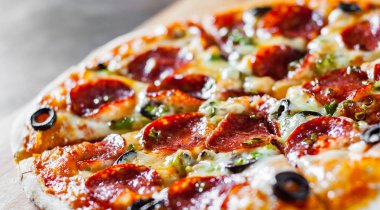 Pizza Mozzarella peyniri, sucuk, domates, biber, zeytin, salam. Ahşap masa arka plan üzerinde İtalyan pizza