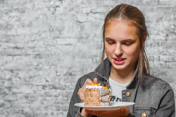 灰色の壁の背景にスライス ケーキ デザートを食べて長い髪の 代の若いブルネットの少女の肖像画 — ストック写真
