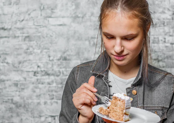 灰色の壁の背景にスライス ケーキ デザートを食べて長い髪の 代の若いブルネットの少女の肖像画 — ストック写真