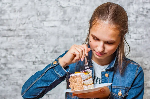 灰色の壁の背景にスライス ケーキ デザートを食べて長い髪の 代の若いブルネットの少女の肖像画 — ストック写真