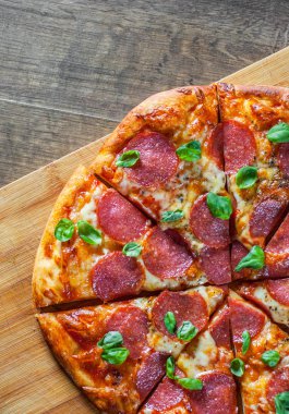 Pepperoni Pizza Mozzarella peyniri, salam, domates, biber, baharat ve taze fesleğen. Ahşap masa arka plan üzerinde İtalyan pizza