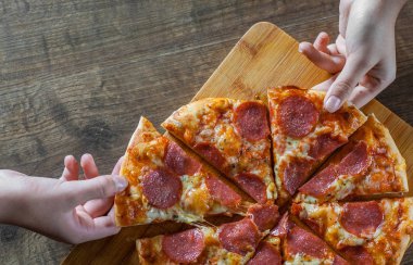 iki kadın elini tutuyor bir dilim biberli Pizza Mozzarella peynir, salam, domates, biber. Ahşap masa arka plan üzerinde İtalyan pizza